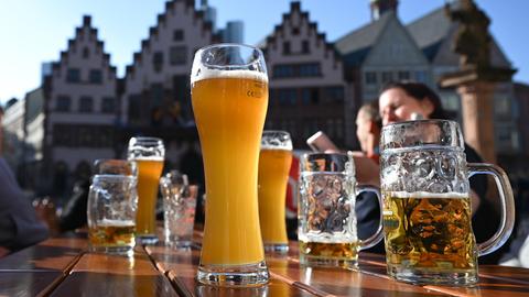 Das Bild zeigt einen Tisch mit Bierkrügen darauf. Im Hintergrund ist der Frankfurter Römerberg zu sehen.
