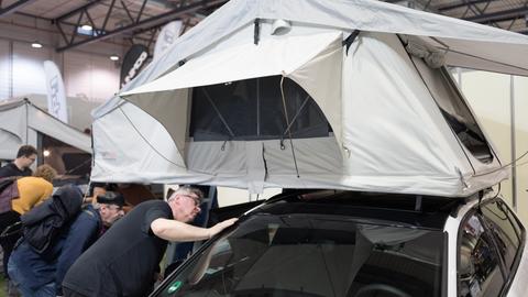 Messe-Besucher betrachten ein Dachzelt auf einem Auto. 