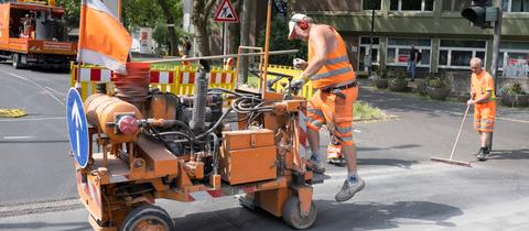 Männer in orangenen Baustellenanzügen richten eine Baustelle ein.