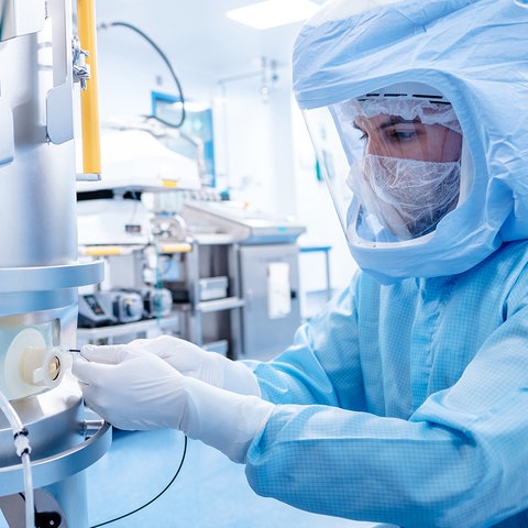 Ein Mensch in Schutzkleidung, die an einen Astronauten erinnert, steht an der Impfstoffproduktionsanlage und arbeitet. 