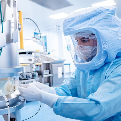 Ein Mensch in Schutzkleidung, die an einen Astronauten erinnert, steht an der Impfstoffproduktionsanlage und arbeitet. 