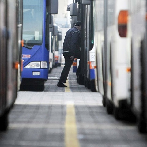 Foto von vielen Bussen, die in Reihen stehen (unscharf). Dazwischen ein Busfahrer, der in einen Bus steigt (scharf).