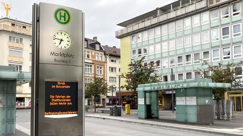 Im Bildvordergrund linke eine Stele einer Bushaltestelle mit der Anzeige "Streik im Busverkehr - Die Fahrten der Stadtbuslinien fallen heute aus, die Regionalbusse fahren." Im Hintergrund eine menschenleere Bushaltestelle im städtischen Umfeld.