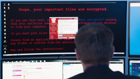 Ein Mann sitzt vor mehreren Computerbildschirmen. Auf einem steht der englische Text: "Ooops, your important files have been encrypted" zu lesen. 