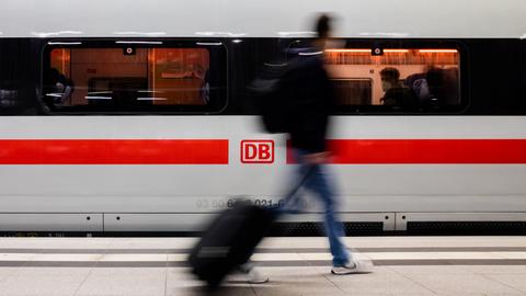 Auf einem Bahnsteig läuft ein Mensch mit Gepäck (unscharf) an einem ICE (scharf) entlang.