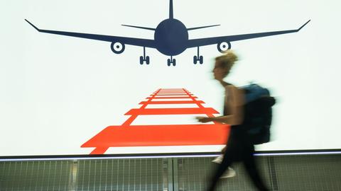 Eine Frau geht auf dem Frankfurter Flughafen am Rande des Fernbahnhofes an einer Werbetafel vorbei, die für das kombinierte Reisen mit Bahn und Flugzeug wirbt.