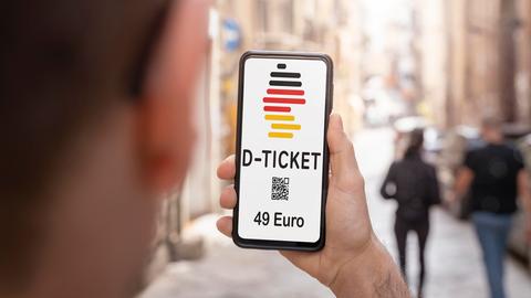 Mann hält ein Handy mit einem digitalen Deutschlandticket hoch