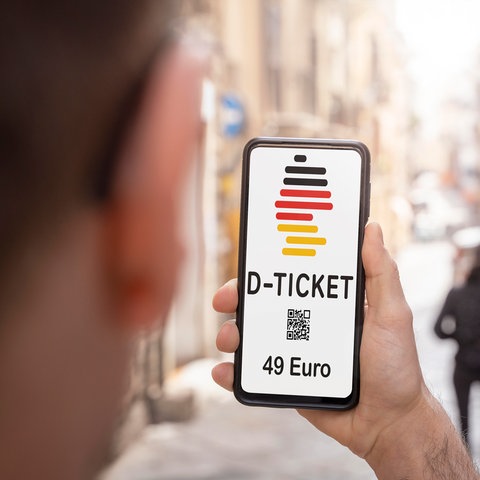 Mann hält ein Handy mit einem digitalen Deutschlandticket hoch