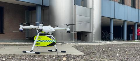 Eine Drohne mit vier Rotoren hat unter dem Motor eine neongelbe Transportkiste für Gewebeproben oder Medikamente.