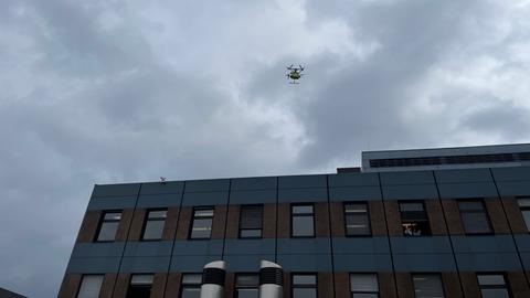 Eine Drohne mit einer Transportkiste für Gewebeproben oder Medikamente fliegt über einem Gebäude am Klinikum Kassel