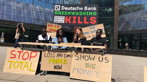 Luisa Neubauer sitzt an einem Tisch vor der Deutschen Bank und protestiert gegen Greenwashing.