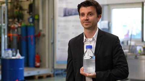 Ein Mann hält eine Flasche mit einer durchsichtigen Flüssigkeit in der Hand.