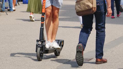 Ein Man fährt auf einem gemieteten E-Scooter durch eine belebte Fußgängerzone.