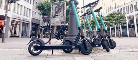 Vier E-Scooter stehen gruppiert in einer Fußgängerzone.