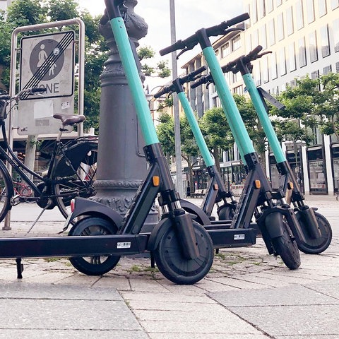 Vier E-Scooter stehen gruppiert in einer Fußgängerzone.