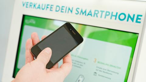 Eine Hand hält ein Smartphone vor den Bildschirm eines Automaten, auf dem steht: "Verkaufe dein Smartphone"