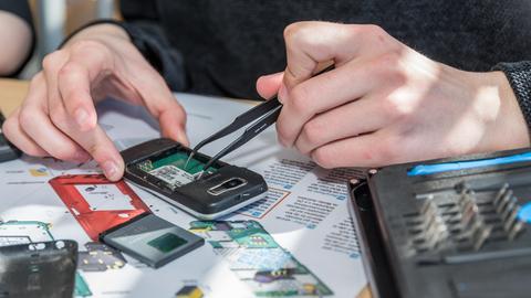 Jemand baut ein Smartphone auseinander, man sieht eine Hand mit einer Pinzette, die Teile aus dem Gerät holt.