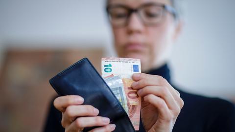 Eine blonde Frau zieht Geldscheine aus einem Portemonnaie