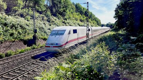 Ein ICE fährt auf Gleisen, umgeben von Gebüsch und erdigen Hängen.