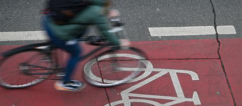 Ein Radfahrer ist in der Innenstadt auf einer roten Fahrradspur unterwegs (Aufnahme mit längerer Verschlusszeit).