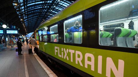 Ein leuchtend grüner Zug hält an einem Bahnhof, darin sind Fahrgäste.