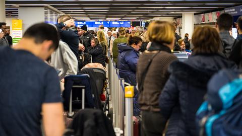 Viele Menschen mit Koffern stehen in Schlangen am Flughafen