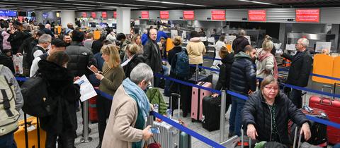 Viele Menschen mit Koffern stehen an Check-In-Schaltern am Flughafen