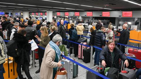 Viele Menschen mit Koffern stehen an Check-In-Schaltern am Flughafen