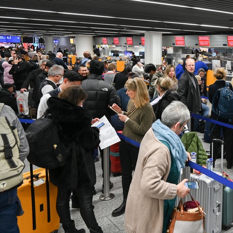 Viele Menschen mit Koffern stehen an Check-In-Schaltern am Flughafen
