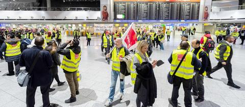 Streikende Verdi-Mitglieder in gelben Westen in einer großen Flughafenhalle.
