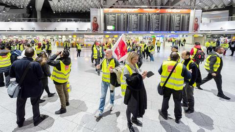Streikende Verdi-Mitglieder in gelben Westen in einer großen Flughafenhalle.