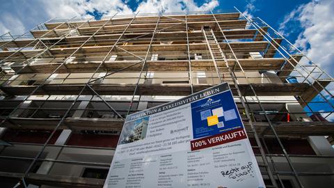 Vor einem Mietshaus steht ein Baugerüst mit einem Werbeplakat, welches für die Wohnlage wirbt.