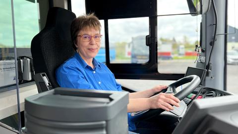 Ein Frau sitzt in einem Führerhaus eines Busses hinter dem Lenkrad und lacht in die Kamera.