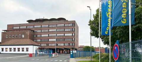 Industriegebäude mit blauen Fahnen davor, auf denen in gelben Lettern "Goodyear" steht.