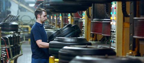 Ein Mann steht in einer Industriehalle an einer Maschine und arbeitet an einem Reifen.