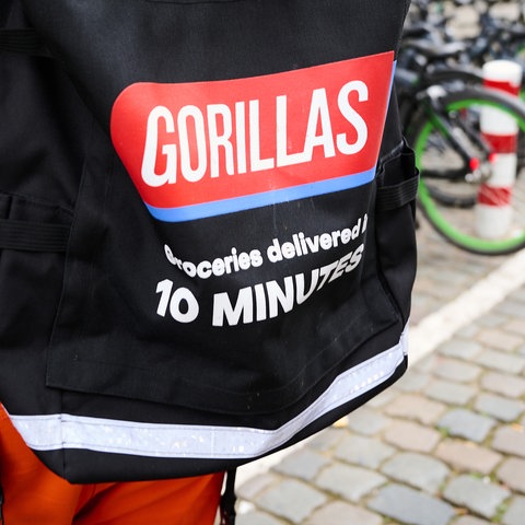 Radfahrer von hinten, der am Fahrradparkplatz steht. Auf seinem Rücken ein schwarzer Rucksack mit der Aufschrift "Gorillas - geliefert in 10 Minuten".