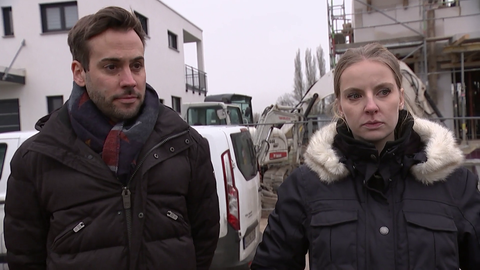 Ein Mann und eine Frau stehen mit ernsten Gesichtern auf einer Baustelle.