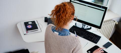 Eine Frau arbeitet in ihrer Wohnung vor einem Computer an einem Schreibtisch.
