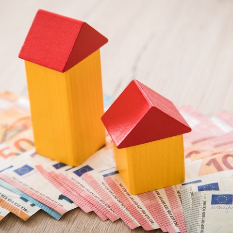 Symbolbild Immobilienfinanzierung - Holzbauklötze in Häuschenform stehen auf Euro-Banknoten