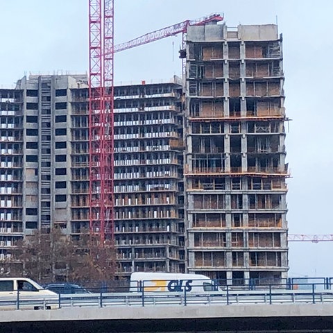 Blick auf eine Baustelle mit Gebäuden noch im Rohzustand. Davor verläuft eine Brücke mit zwei Autos.