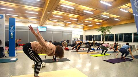 Menschen machen gemeinsam Yoga-Übungen in einem Flughafengebäude