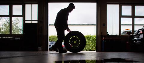 Ein Mann rollt einen Reifen durch eine Werkstatt, Scherenschnitt