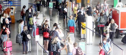 Menschen mit Koffern warten in einer langen Schlange in einer Flughafenhalle (von oben fotografiert).