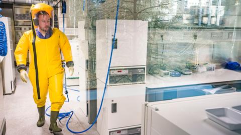 Ein Mitarbeiter in einem gelben Schutzanzug arbeitet in einem Labor an Organismen im Hochsicherheitsbereich des Instituts für Virologie der Philipps-Universität Marburg. 