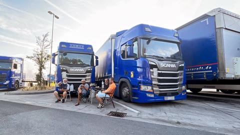 Vier Männer sitzen auf Campingstühlen vor Lastwagen auf einer Raststätte.