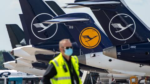 Ein Mann mit Mundschutzmaske steht vor Lufthansa-Maschinen,