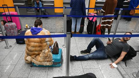 Eine Frau sitzt auf ihrem Koffer, ein Mann liegt auf dem Boden zwischen blauen Absperrbändern.