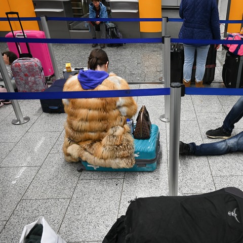 Eine Frau sitzt auf ihrem Koffer, ein Mann liegt auf dem Boden zwischen blauen Absperrbändern.