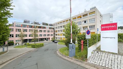 Außenansicht eines Krankenhausgebäudes. Einfahrt und Eingang mit Schranke und Schild