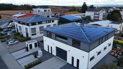 Solarzellen auf dem Dach eines Gebäudes, daneben E-Ladesäulen.
